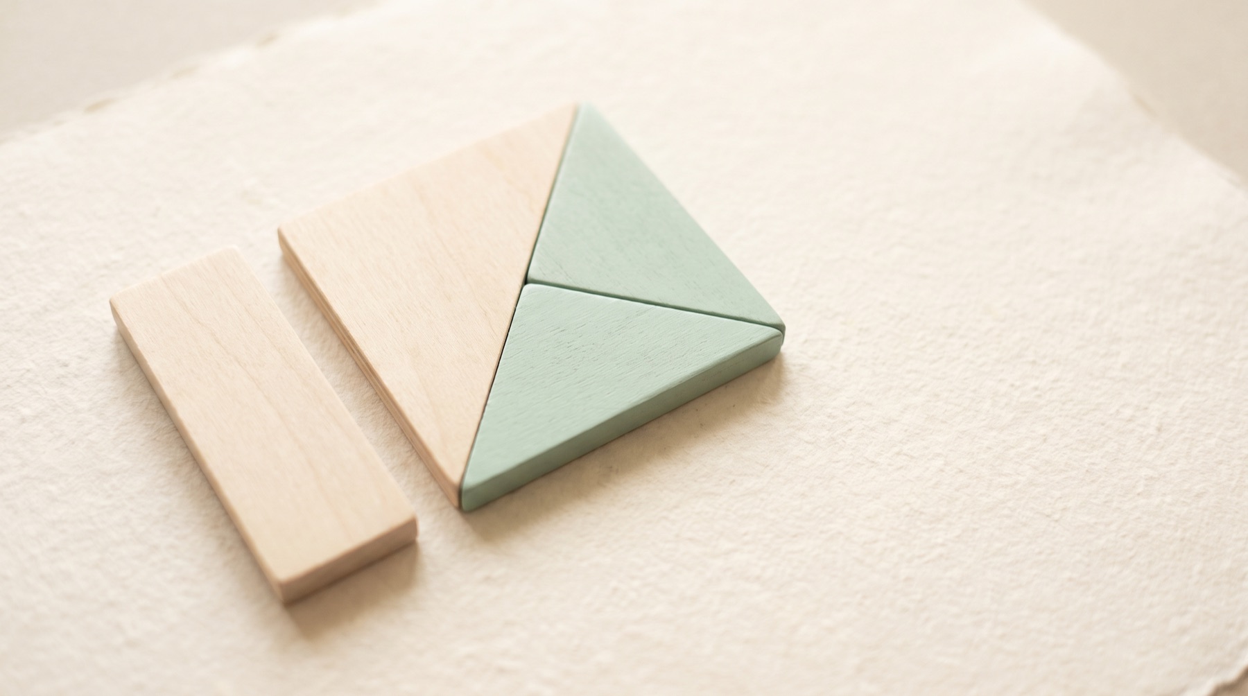 Wooden geometric tiles on warm paper, two fitted together and one set apart.